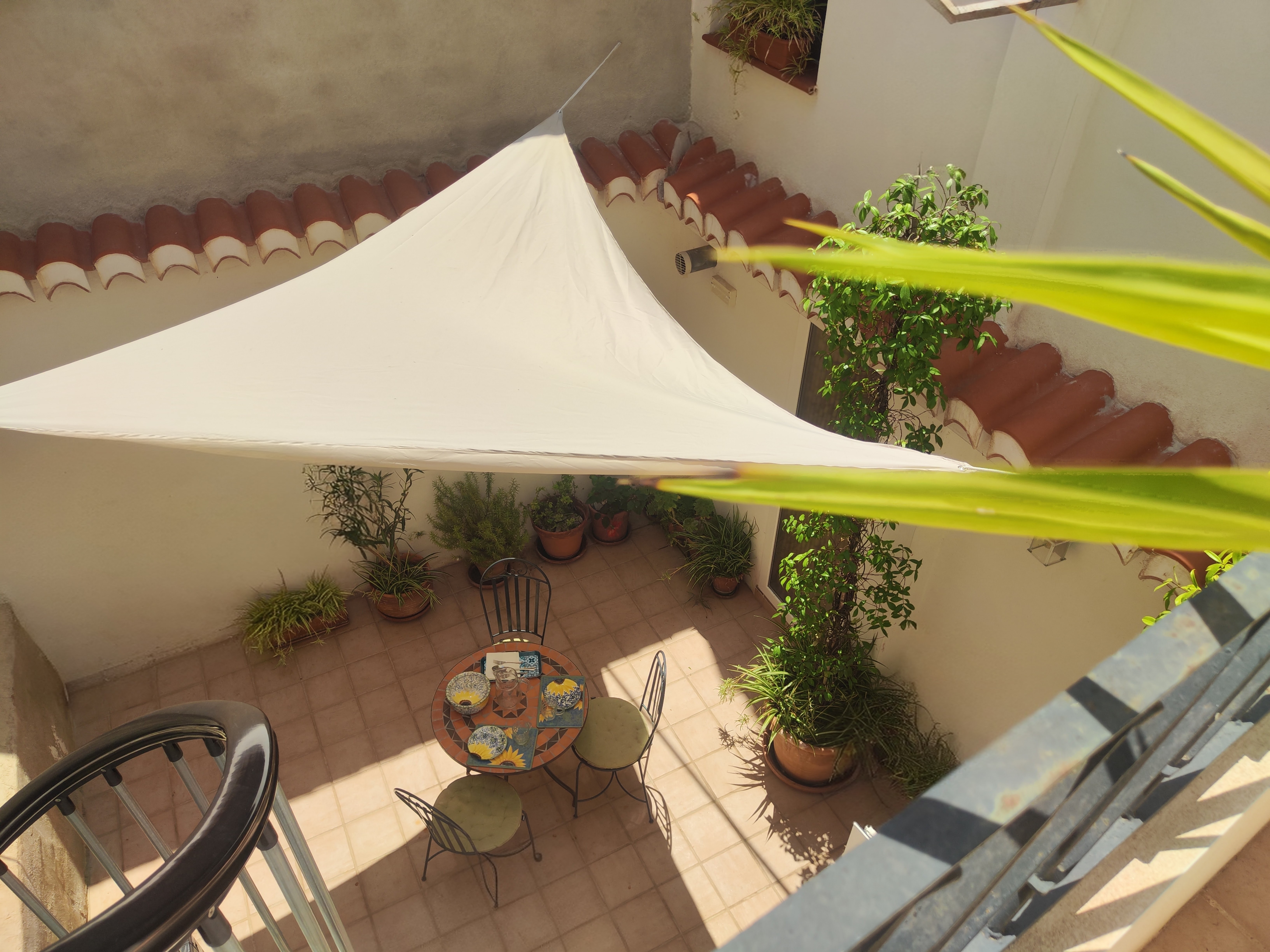 Blik op de sfeervolle patio van Casita Klein Zwitserland vanaf de wenteltrap naar het dakterras, met mozaïektafel, planten en Andalusische details