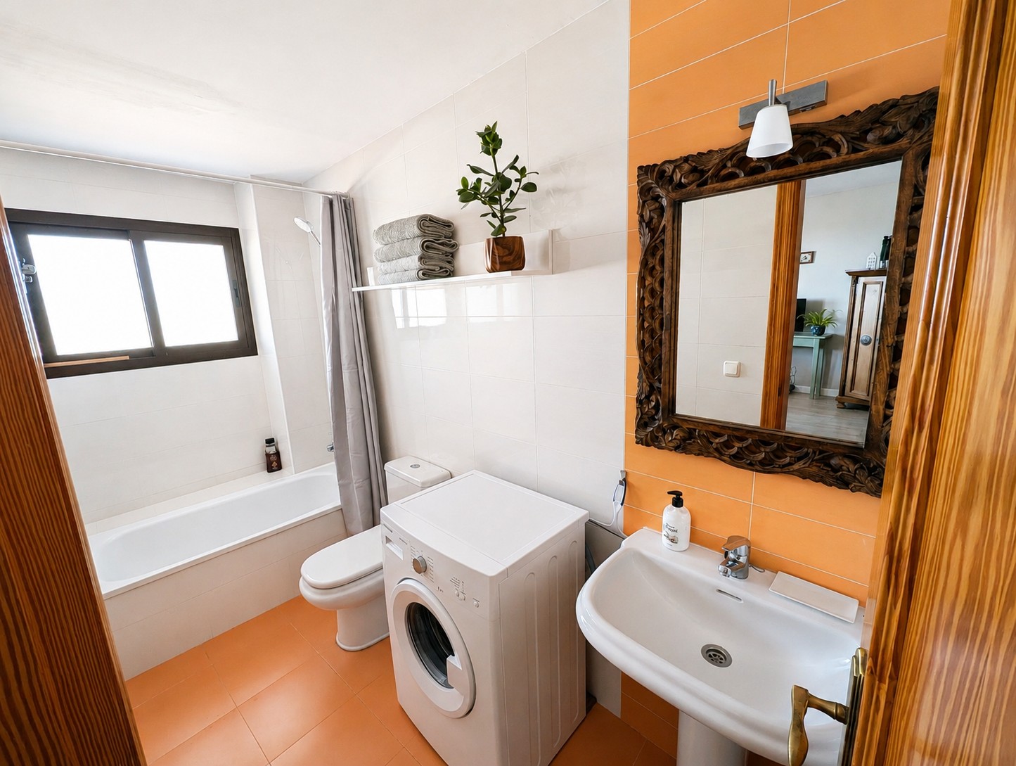 Badkamer van Ático Lolapaluza met badkuip, wastafel, wc, wasmachine en decoratieve houtsnijwerk spiegel