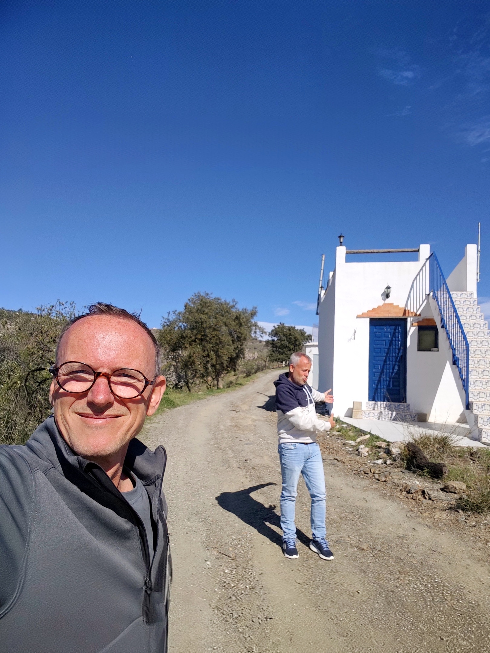 Selfie van Reijer en Johan bij een cortijo in La Contraviesa in La Alpujarra met wit huis, blauwe deur en dakterras tussen groene bomen
