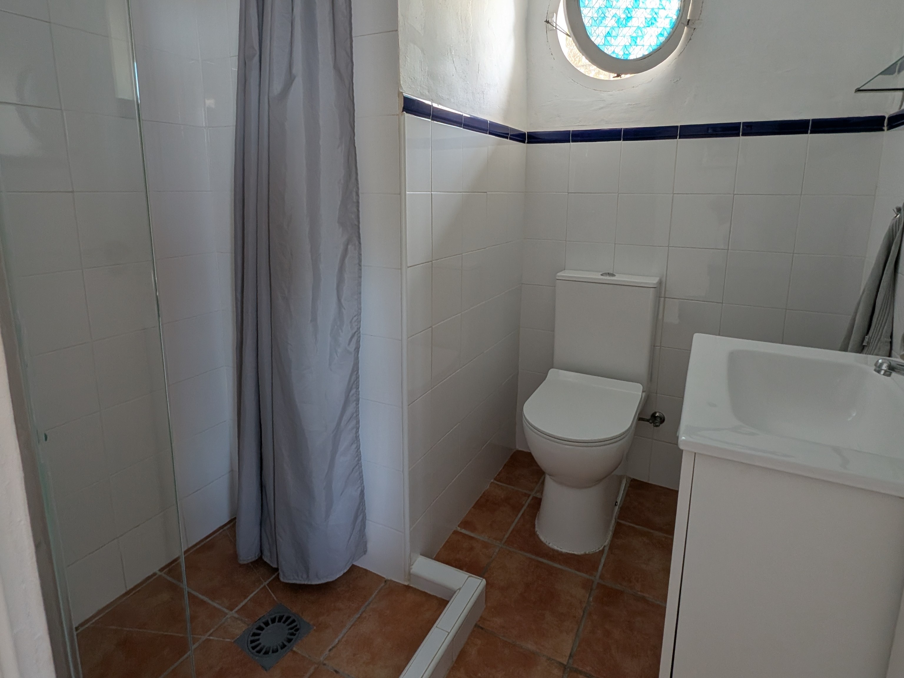 De inloopdouche van de compacte badkamer in Villa Merise, met witte en blauwe tegels in Spaanse retrostijl. De doucheruimte is praktisch ingericht en voorzien van een moderne douchekop