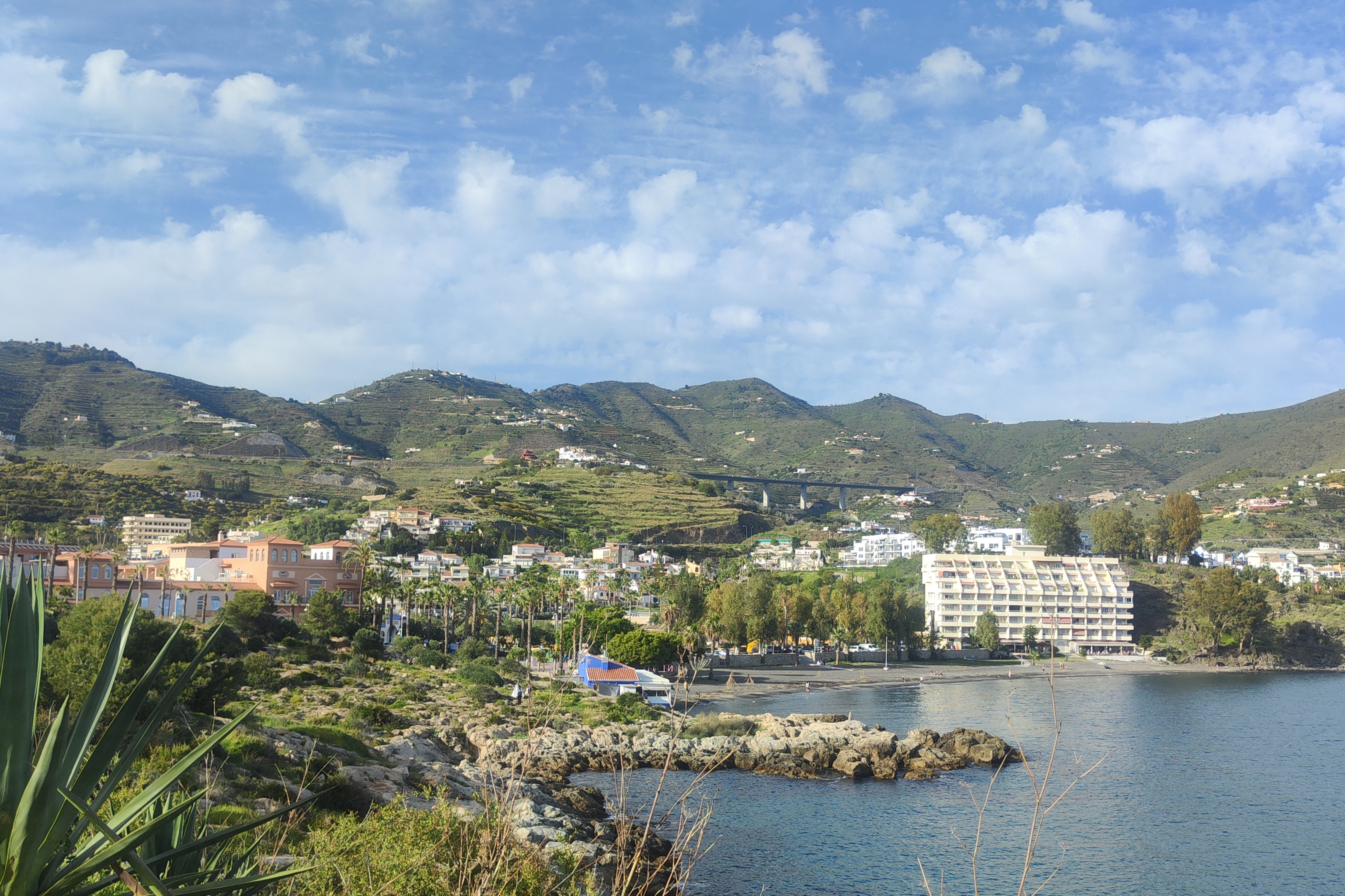 Panoramisch uitzicht vanaf Torre del Tesorillo richting Barrio de Taramay, met op de voorgrond Playa de Pozuelo en het park, daarachter woonwijk Taramay en de groene heuvels van het achterland van Almuñécar, Costa Tropical