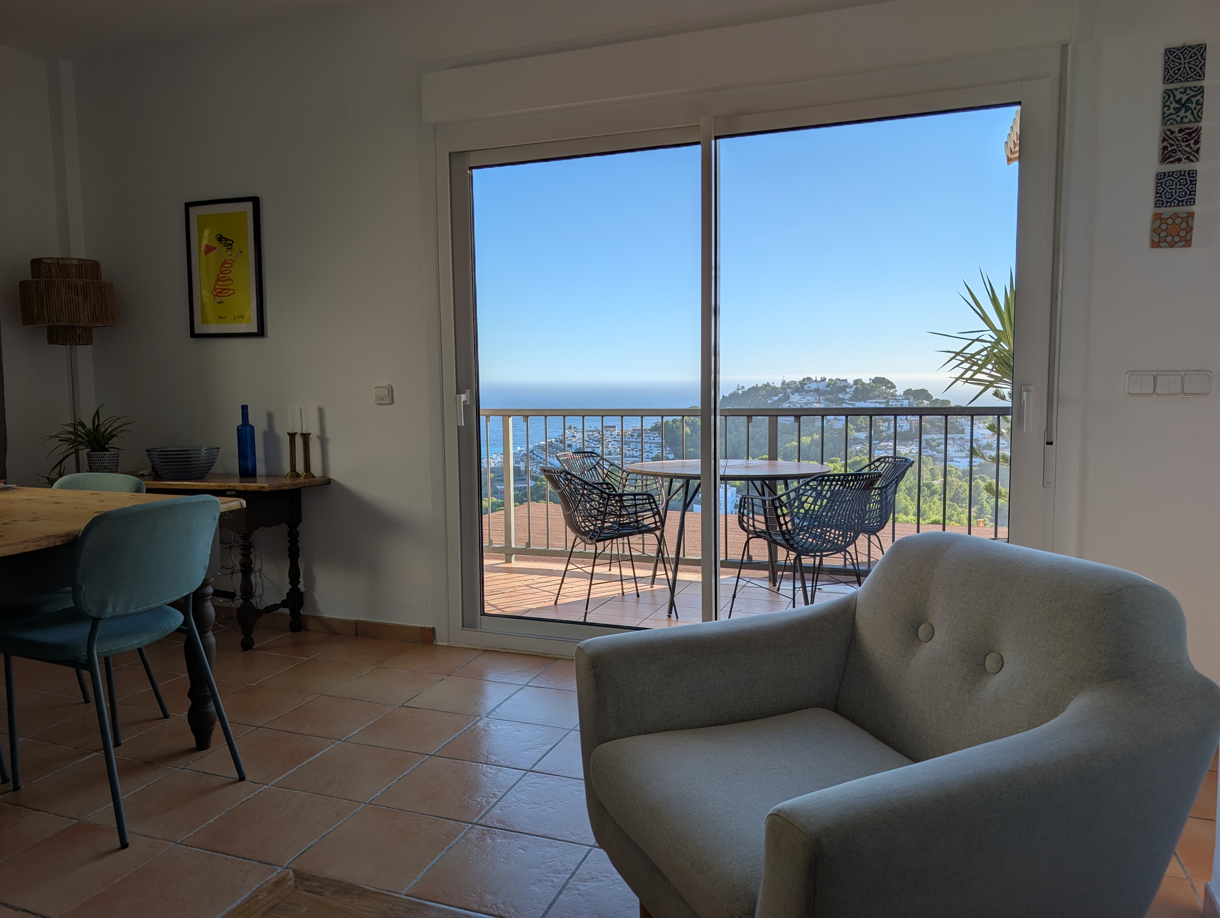 Gezellige woonkamer in Fuentes de Almuñécar, gefotografeerd vanaf de loungebank. Te zien zijn de sfeervolle eethoek, een rustieke salontafel, veel natuurlijke lichtinval en de schuifpui naar het terras met zeezicht.