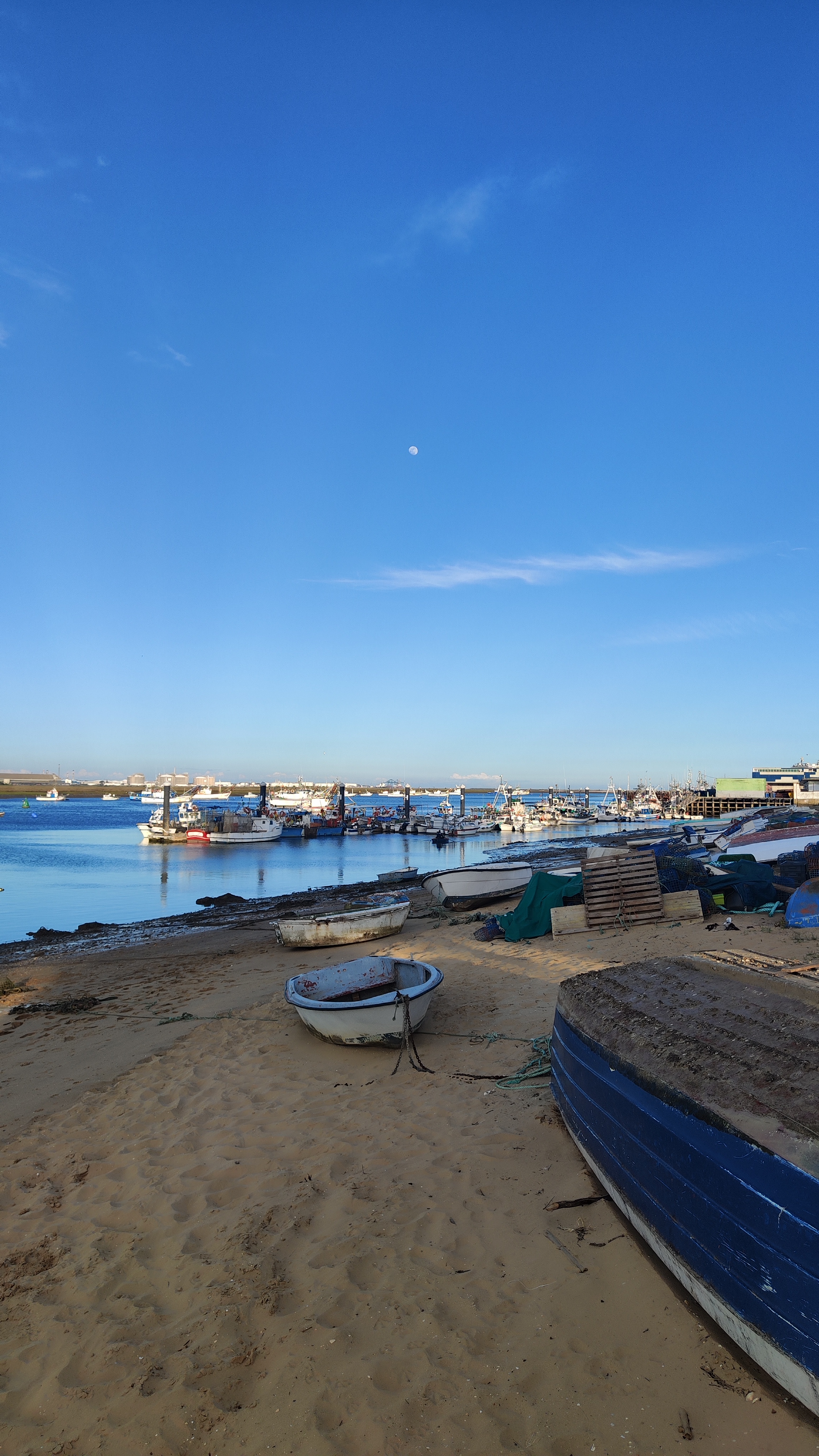 De lagune bij Punta Umbría (Huelva) met visserboten aan de oever en op het water. Een eenzame roeier vaart onder de volle meimaan, die al hoog aan de hemel staat.