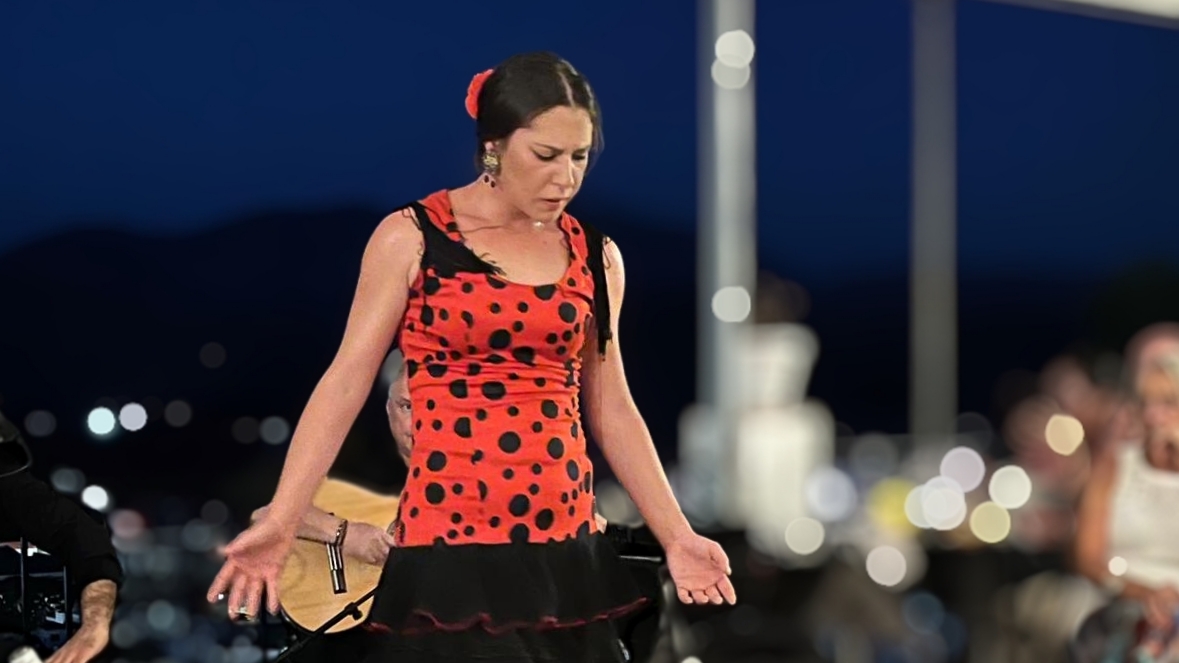 Victoria Macías Costela, flamencodanseres, dansend in Restaurante La Traviesa met een intense blik naar beneden en armen in een open, ontvangende pose.