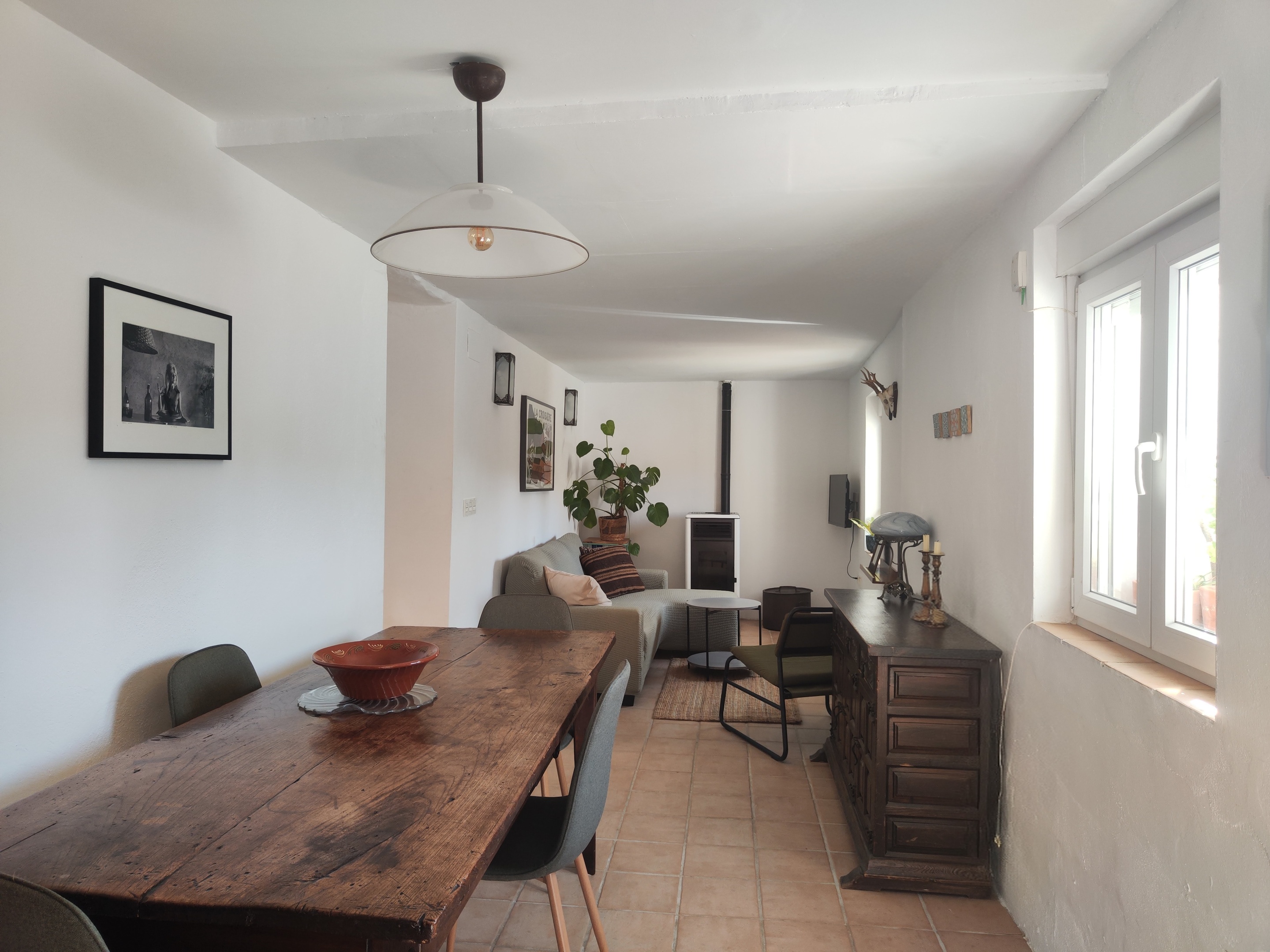 Sfeervolle woonkamer van Casita Klein Zwitserland in de Lecrínvallei, met antieke kasteeltafel, buffetkast, een knusse zithoek met loungebank, pelletkachel voor winteravonden, Perzisch tapijt en kunst aan de muur. Ideale uitvalsbasis om de Alpujarra, Sierra Nevada, Granada en de Costa Tropical te verkennen.