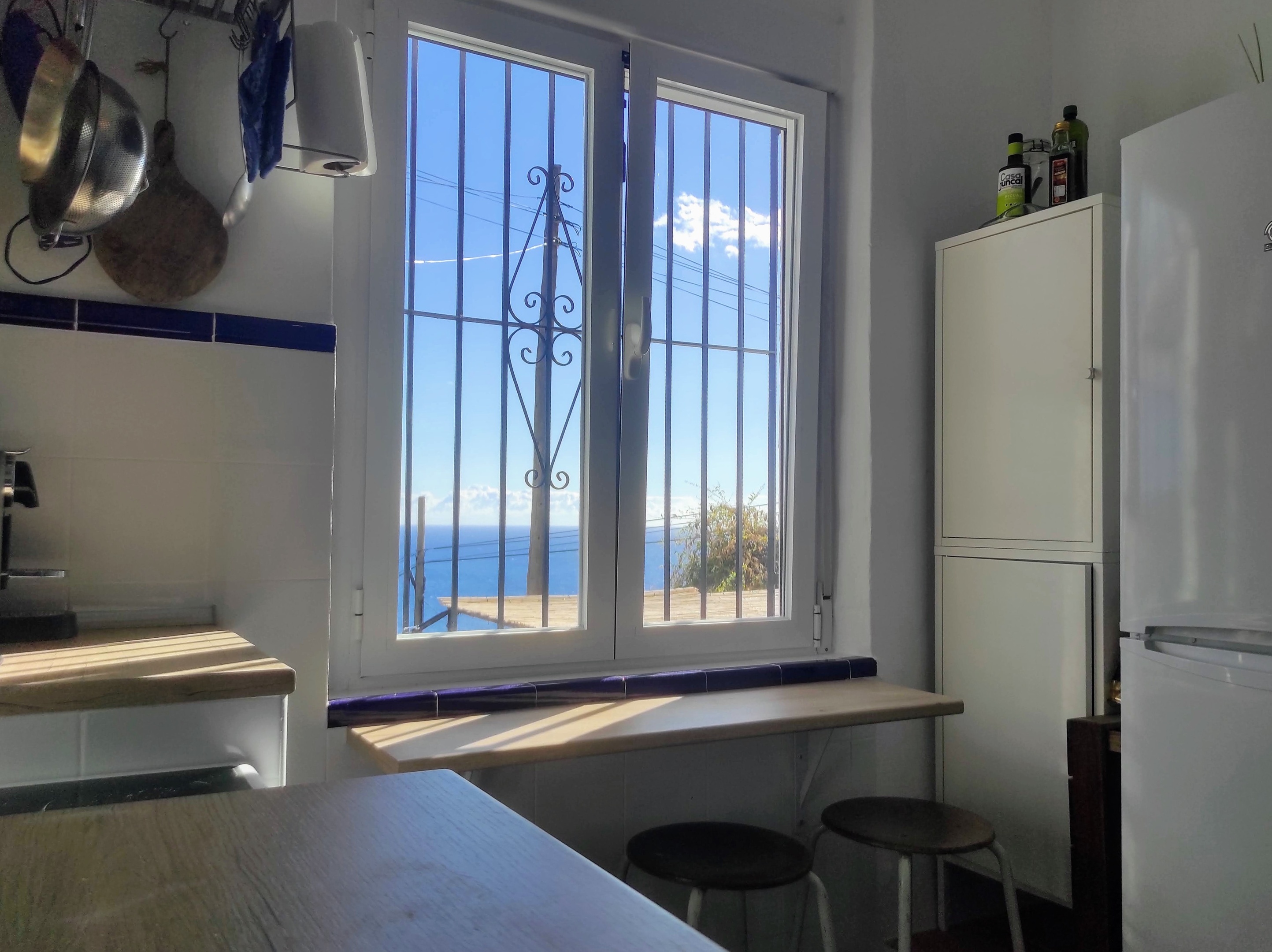 De keuken van Villa Merise, met een groot raam dat uitkijkt op zee, combineert Spaanse retro charme met moderne gemakken. Voorzien van een keramische kookplaat, oven, magnetron, vaatwasser, Nespresso-apparaat, ruime koelkast met vriezer, broodrooster en blender – alles voor een zorgeloos verblijf.