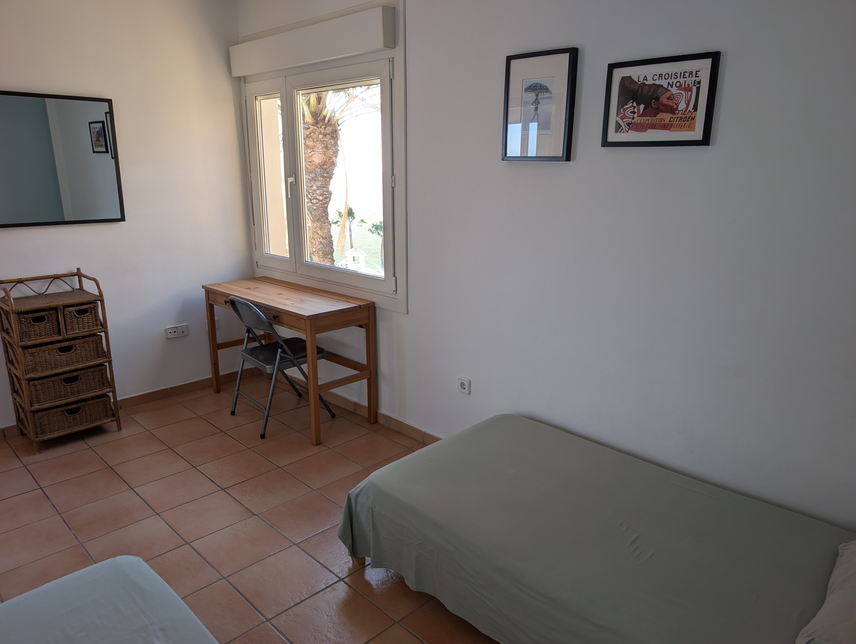 Ander perspectief van de tweede slaapkamer van Casa Larimar, met een focus op het dressoir, het raam met uitzicht op de palmboom en de groene bergen van de Costa Tropical.