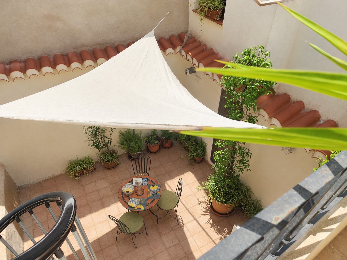 Blik op de sfeervolle patio van Casita Klein Zwitserland vanaf de wenteltrap naar het dakterras, met mozaïektafel, planten en Andalusische details