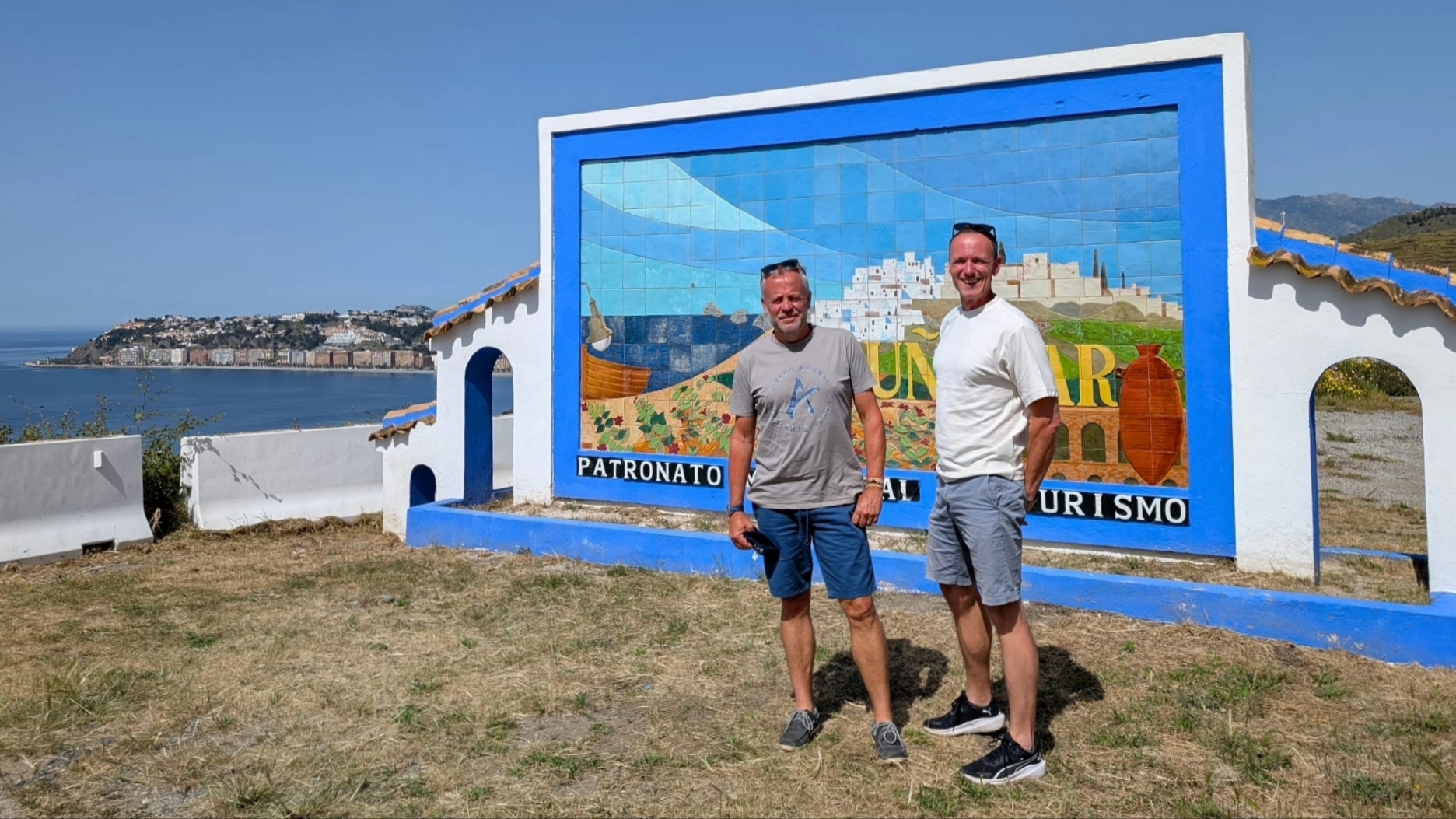 Johan & Reijer onder de zon, voor het kleurrijke billboard van Almuñécar, met zee & stad op de achtergrond.