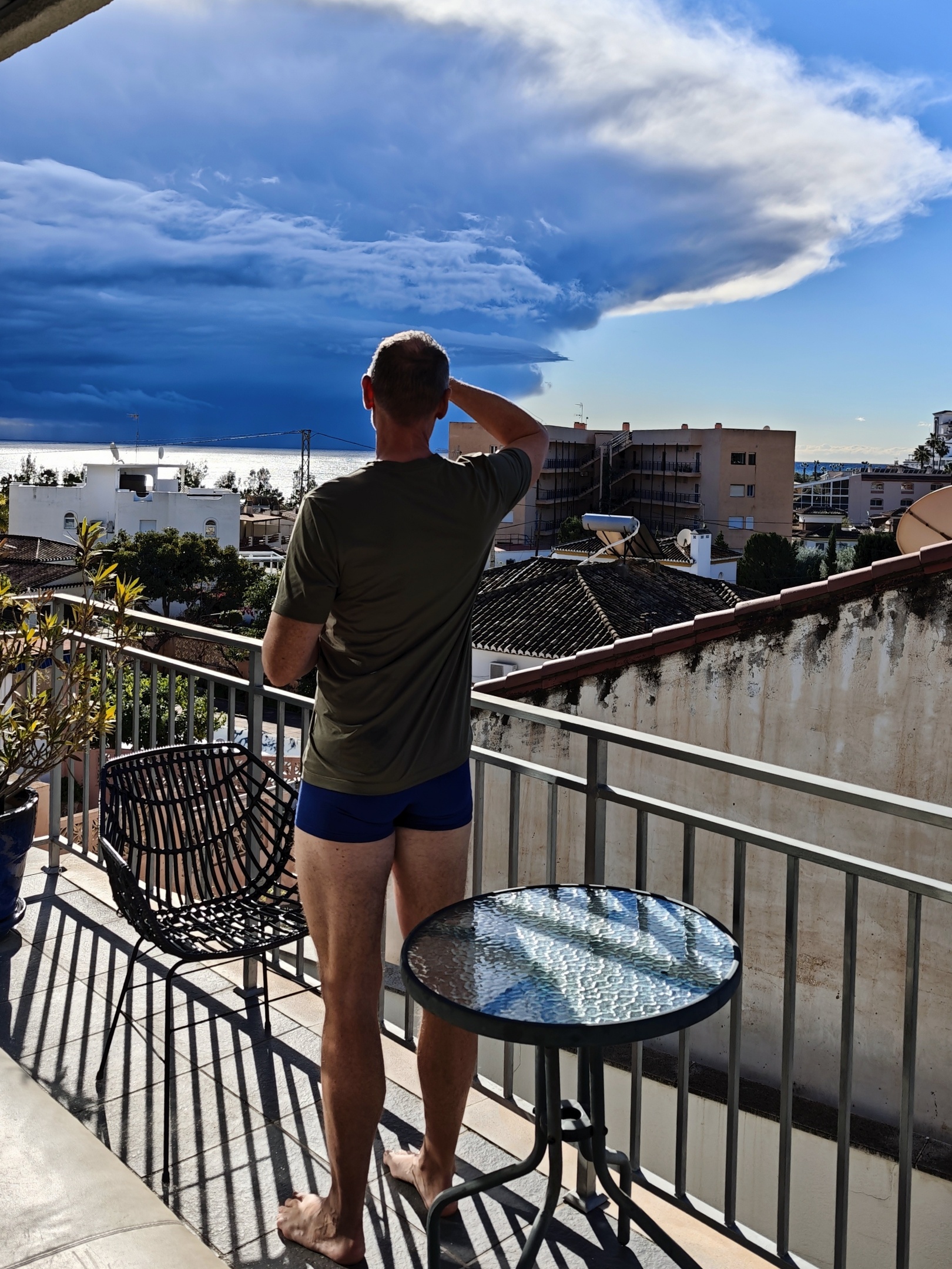 Man op balkon in Andalusië met uitzicht op zee, dreigende onweerslucht aan één kant en blauwe hemel aan de andere kant