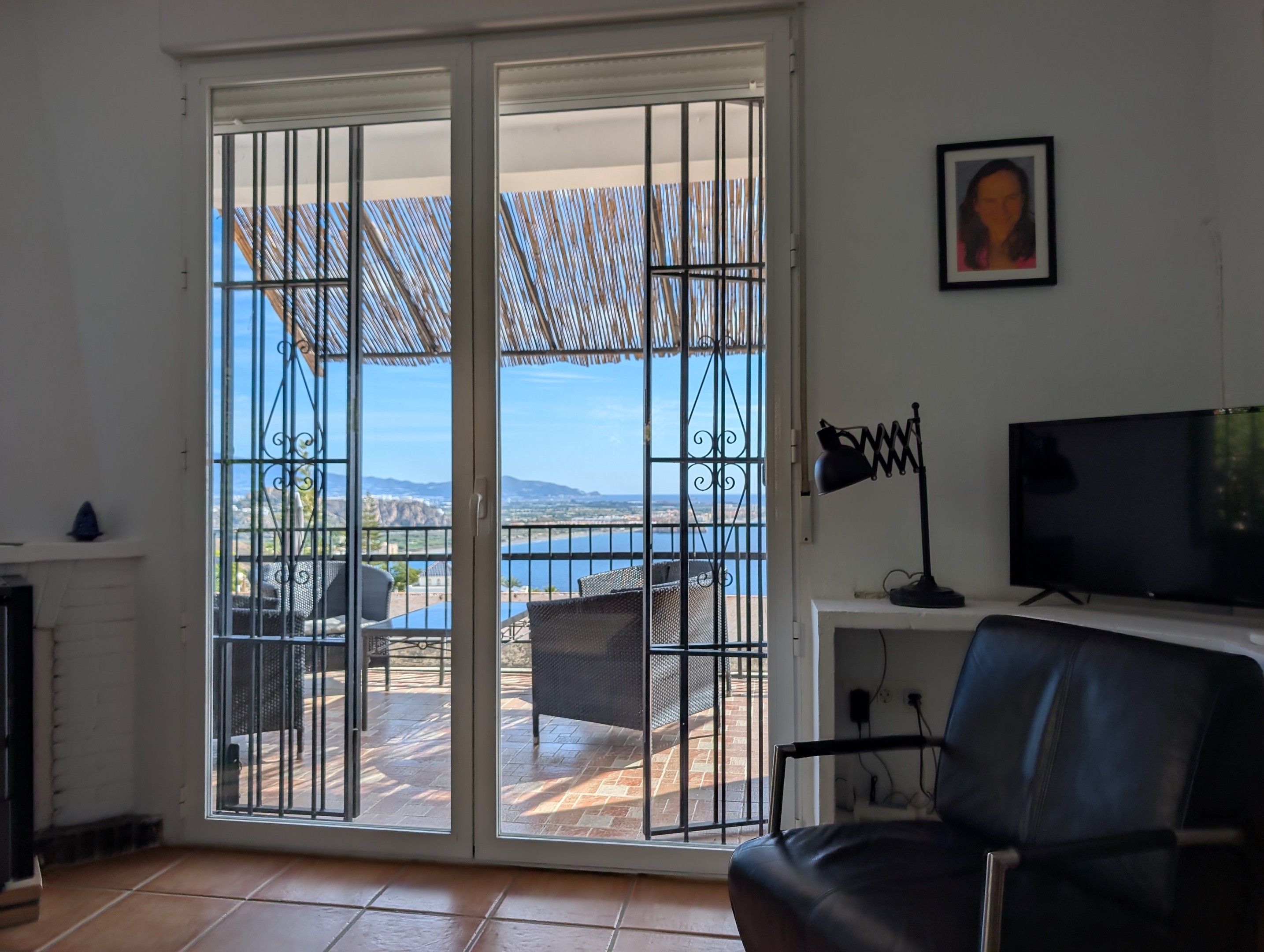 Foto van de woonkamer in Villa Merise vanuit de eethoek: de toegang naar de verandaamers is zichtbaar, evenals de openslaande deuren die naar de veranda en het zeezicht leiden. De rest van de woonkamer, inclusief de comfortabele bank en retrofauteuils, draagt bij aan de ontspannen sfeer van het huis. Villa Merise ligt vlakbij Salobreña, aan de prachtige Costa Tropical