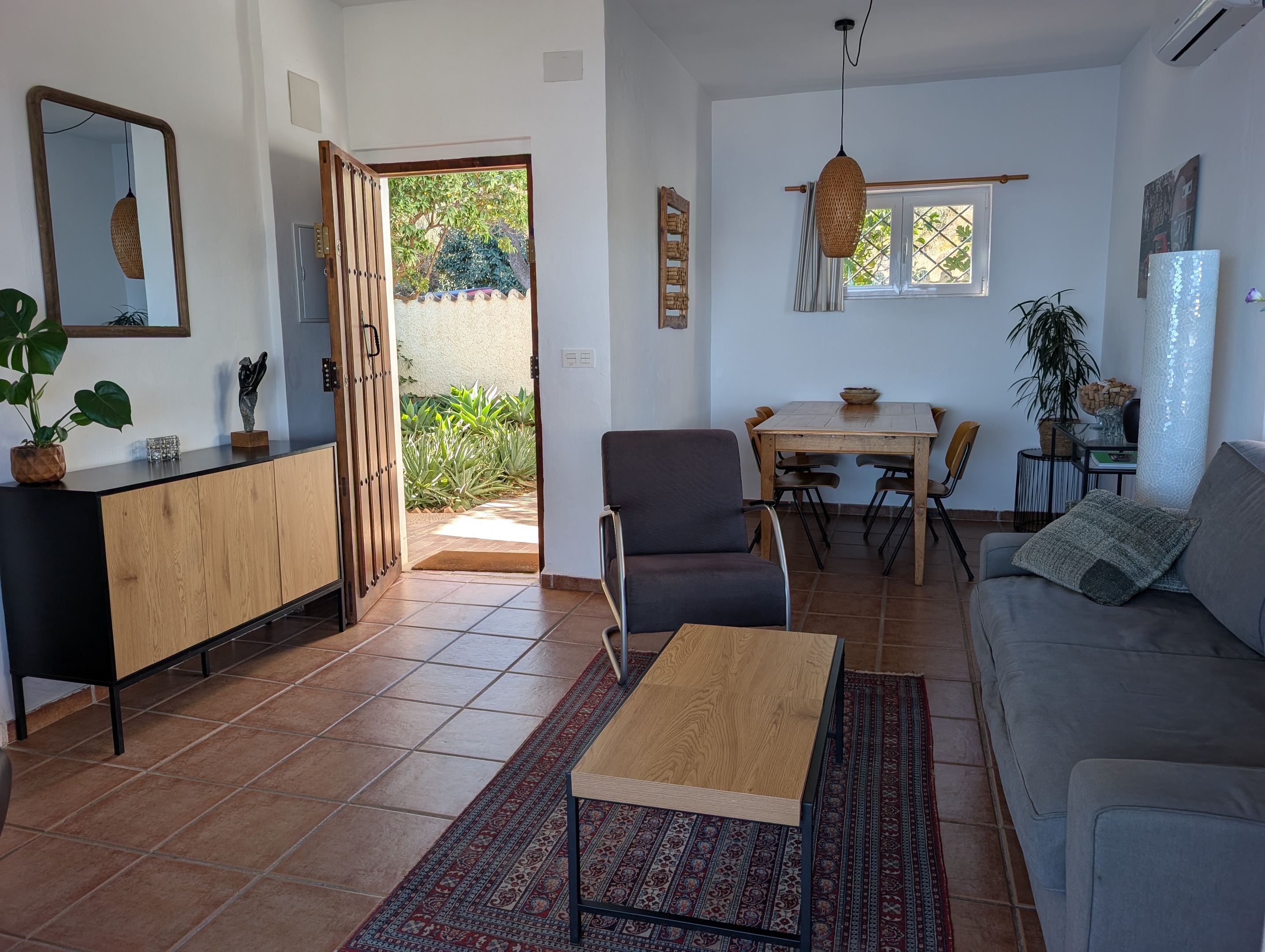 Een blik op de woonkamer van Villa Merise, gezien vanuit de open voordeur. Je ziet het groen in de voortuin en de eethoek binnen. De villa ligt vlakbij Salobreña, ideaal voor uitstapjes naar de Costa Tropical en het historische centrum van de stad